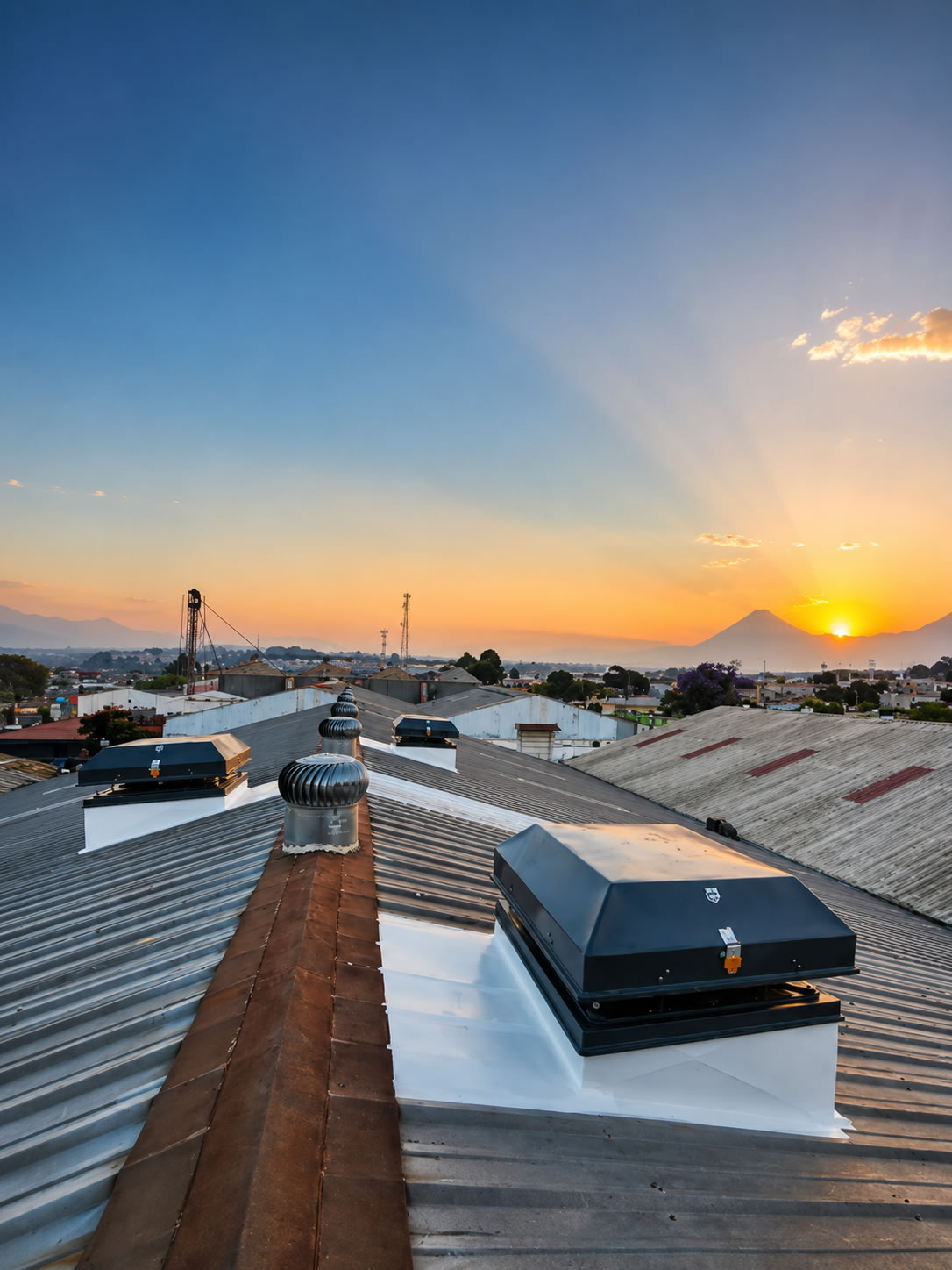 Extractor eólico instalado en techo industrial al atardecer con volcán de fondo